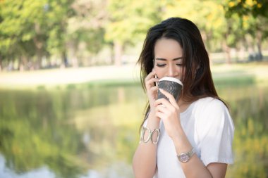 Tek kullanımlık kahve fincanı doğa açık havada kadın yaşam tarzı kavramı telefonla konuşurken tutan genç güzel kadın.