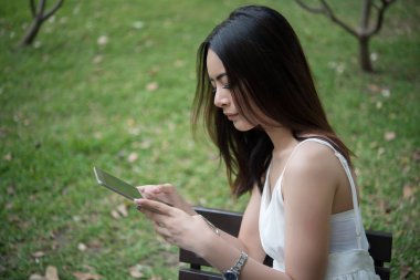 Bir tablet ellerde ile oturan kız. Park onun tablet ile genç rahatlatıcı. Kadın yaşam tarzı kavramı.