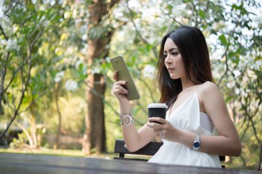Tek kullanımlık kahve fincanı kısa mesaj yoluyla smartphone vasıl doğa açık havada süre tutan genç güzel kadın.