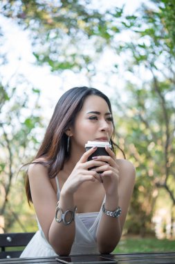 Tek kullanımlık kahve fincanı doğa açık havada oturma tadını çıkarırken tutan genç kadın.