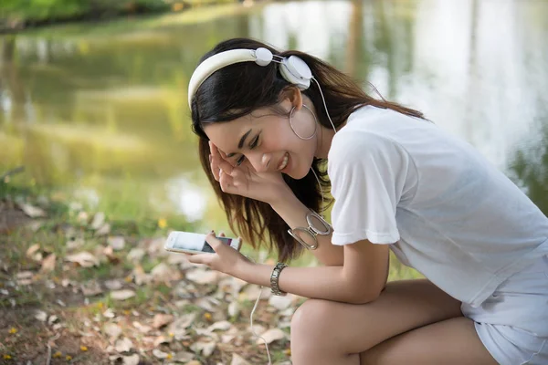 Portrait of a smiling girl with headphones listening to music while relaxing in nature park outdoors.