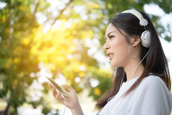 Portrait of a smiling girl with headphones listening to music while relaxing in nature park outdoors.