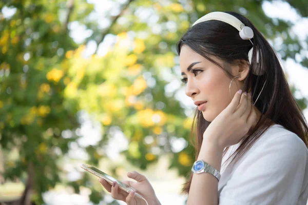 Portrait of a smiling girl with headphones listening to music while relaxing in nature park outdoors.