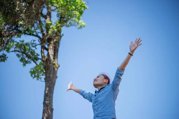 Young woman standing looking to a sky with raised hands while during hike in the mountain.