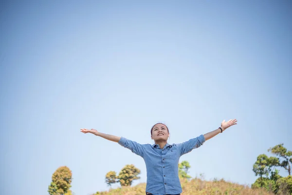 Young woman standing looking to a sky with raised hands while during hike in the mountain.