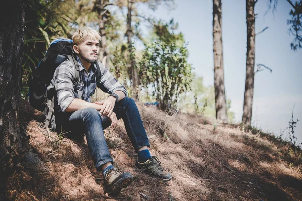 Young tired hiker with backpack sitting on the mountain top while resting after active walk.