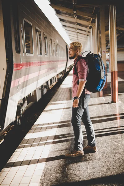 Young hipster tourist with backpack on the train station. Holiday tourist concept.