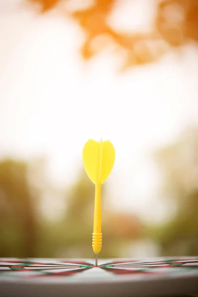 Yellow dart arrow hitting in the center of dartboard.