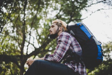 Bir ağaç dalı parkta oturan genç hipster adam