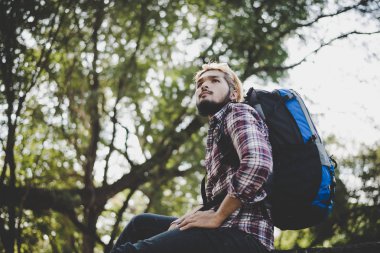 Bir ağaç dalı parkta oturan genç hipster adam