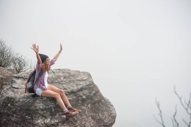 Sırt çantası ile genç hiker cliff ve doğa Vadisi ve dağlar bakarak kenarına oturur.