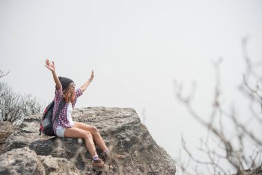 Sırt çantası ile genç hiker cliff ve doğa Vadisi ve dağlar bakarak kenarına oturur.