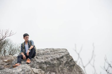 Dağın tepesinde oturan sırt çantası ile genç hipster uzun yürüyüşe çıkan kimse