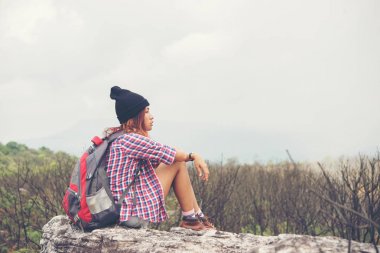 Sırt çantası ile genç hiker cliff ve doğa Vadisi ve dağlar bakarak kenarına oturur.