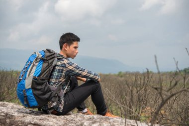 Dağın tepesinde oturan sırt çantası ile genç hipster uzun yürüyüşe çıkan kimse