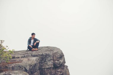 Dağın tepesinde oturan sırt çantası ile genç hipster uzun yürüyüşe çıkan kimse