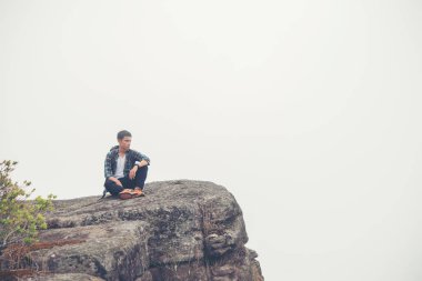 Dağın tepesinde oturan sırt çantası ile genç hipster uzun yürüyüşe çıkan kimse