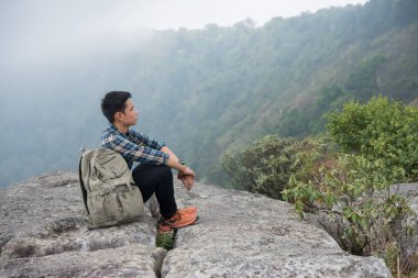 Dağın tepesinde oturan sırt çantası ile genç hipster uzun yürüyüşe çıkan kimse