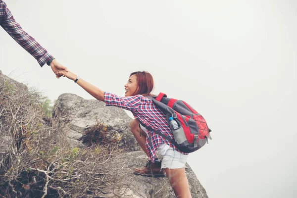 Young hipster man helping woman climbing mountain.