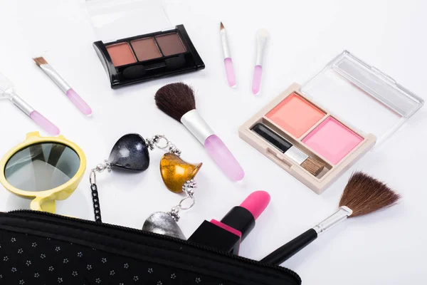 Top view of a make up bag, with cosmetic beauty products spilling out onto a white background.