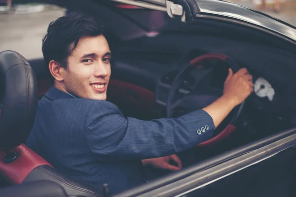 Handsome young man in sports car wearing suit.