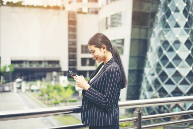 Genç Asyalı işkadını hareket eden smartphone kullanarak. Şehrin büyük bina önünde genç kadın profesyonel.
