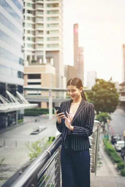 Young asian businesswoman using at mobile smartphone.Young female professional in the city in front of big building.