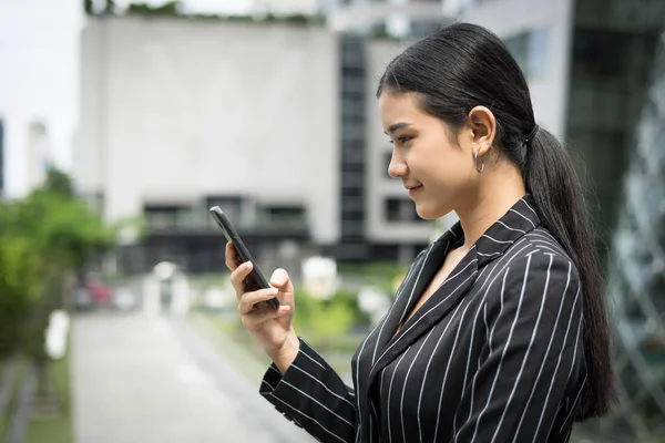 Young asian businesswoman using at mobile smartphone.Young female professional in the city in front of big building.