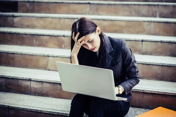 Young business woman stressed from work sitting staircase take a look on her laptop.