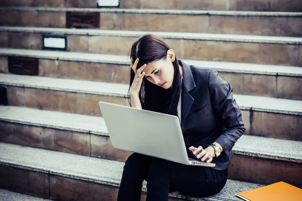 Young business woman stressed from work sitting staircase take a look on her laptop.