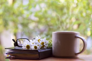 Kupa, papatyalar, not defteri, gözlük. Güneşli yaz sabahı kavramı.