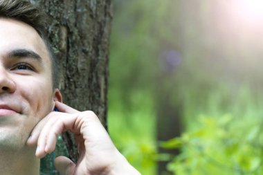 Genç bir adam bir ağacın altında oturuyor ve müzik dinliyor