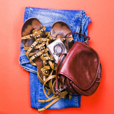 Kot pantolon, sandalet, çantası, fotoğraf makinesi kırmızı zemin üzerine.