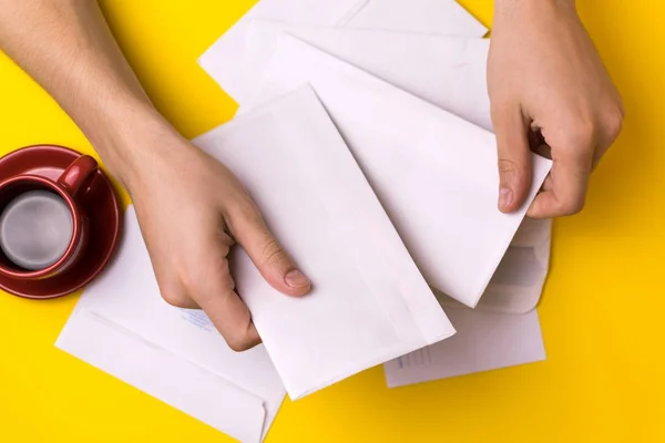 Un hombre ordena el correo. Hombre manos los sobres sobre un fondo amarillo, una taza de café rojo . — Foto de Stock