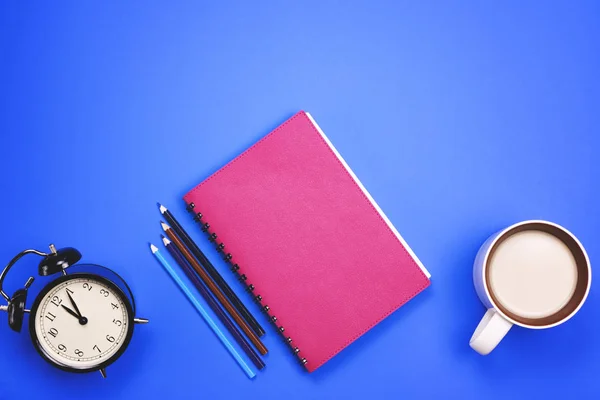 Reloj despertador, cuaderno, lápices sobre fondo azul — Foto de Stock