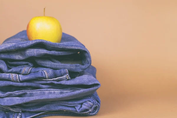 Kvinnors jeans viks i en hög, och ovanpå Apple, på en färgad bakgrund. Gjort i en vintage prestanda. — Stockfoto
