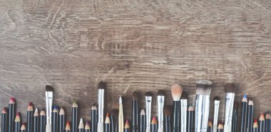 Kozmetik fırçalar ve kalemler ahşap kahverengi bir zeminde yatıyor.