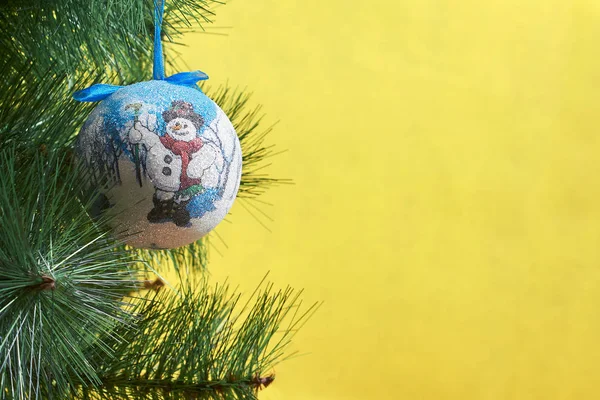 Kugel hängt an einem Fichtenzweig, Weihnachtsbaumspielzeug auf gelbem Hintergrund. — Stockfoto