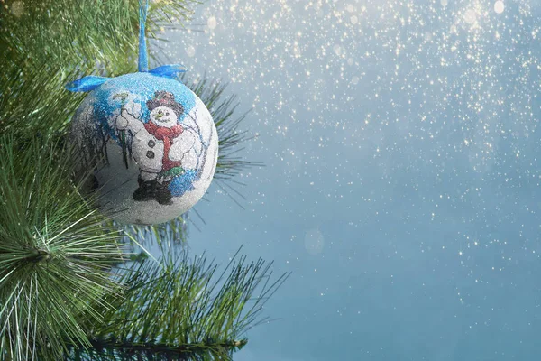 Die Kugel hängt an einem Tannenzweig, ein Weihnachtsbaumspielzeug auf blauem Hintergrund mit Lichtern. — Stockfoto