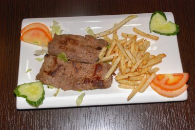 Kızarmış sığır filetosu, yanında patates kızartması ve taze sebze. 