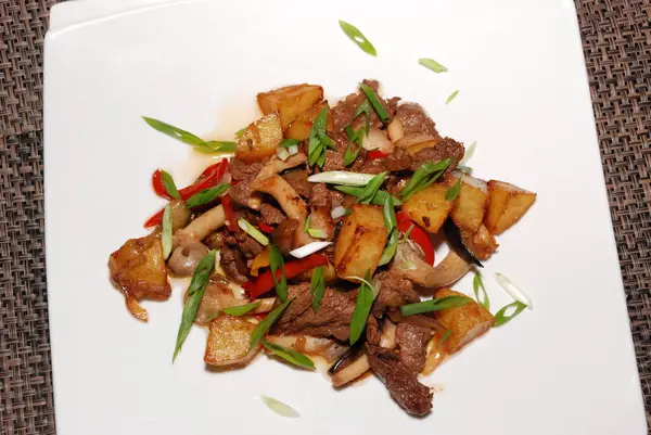 Kızarmış sığır eti, yeşil soğanlı ve beyaz tabakta patates.