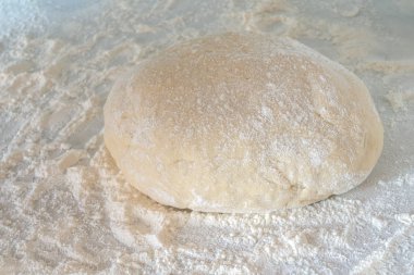 Bir parça çiğ hamur masanın üzerinde biraz un ile birlikte yatıyor. Sıkıca yoğurulmuş bir hamur parçası. Hamur köftesi için gübre.