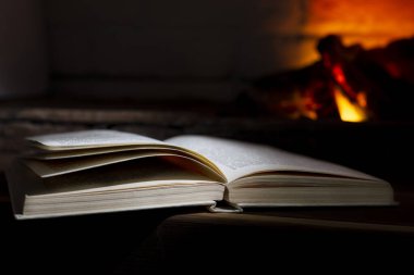 Yanan bir şöminenin yanında açık bir ciltli kitap yatıyor.
