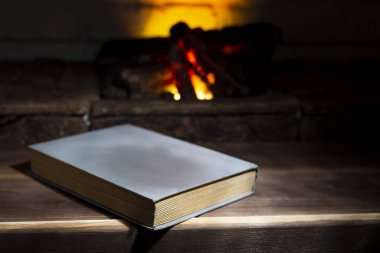 Yanan bir şöminenin yanında açık bir ciltli kitap yatıyor.