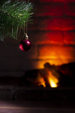 Yanan bir şöminenin arka planında kırmızı topları olan bir Noel ağacı dalı.