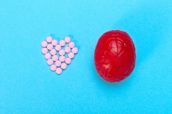 Cérebro vermelho num fundo azul com comprimidos cor de rosa. Alguns comprimidos para o cérebro. Isto é simbólico para drogas, psicofármacos, nootrópicos e outras drogas . — Fotografia de Stock