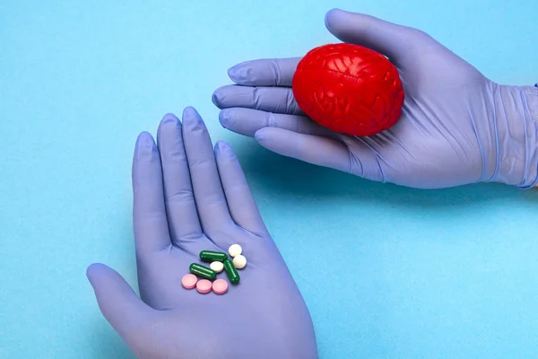 Cerebro rojo sobre fondo azul con pastillas en las manos de un médico. Unas pastillas para el cerebro. Esto es simbólico para las drogas, psicofármacos, nootrópicos y otras drogas. . — Foto de Stock