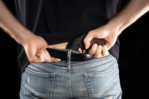 Mann versteckt Waffe hinter Hosengürtel auf schwarzem Hintergrund — Stockfoto