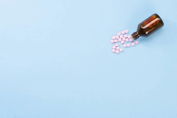 Pastillas rosadas y frasco de vidrio sobre un fondo azul. Concepto de salud y pastillas. Vista plana desde arriba. Copyspace para texto — Foto de Stock