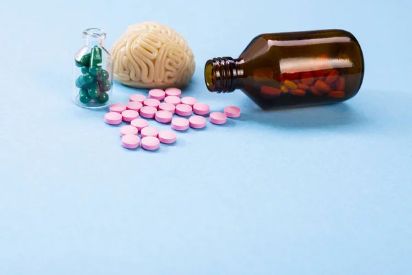 Cérebro em um fundo azul com pílulas rosa e verde em uma garrafa de vidro. Alguns comprimidos para o cérebro. Símbolo para medicamentos, psicofármacos, nootrópicos e outros medicamentos. Medicina. Tratamento cerebral — Fotografia de Stock
